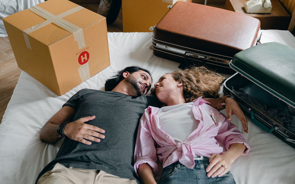 Man and a woman lying on a bed surrounded by suitcases